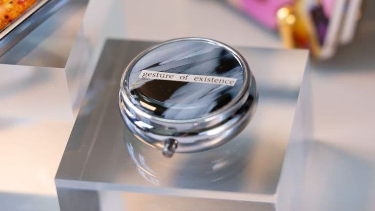 a pillbox with the phrase "gesture of existence," blending scientific imagery with artistic design.