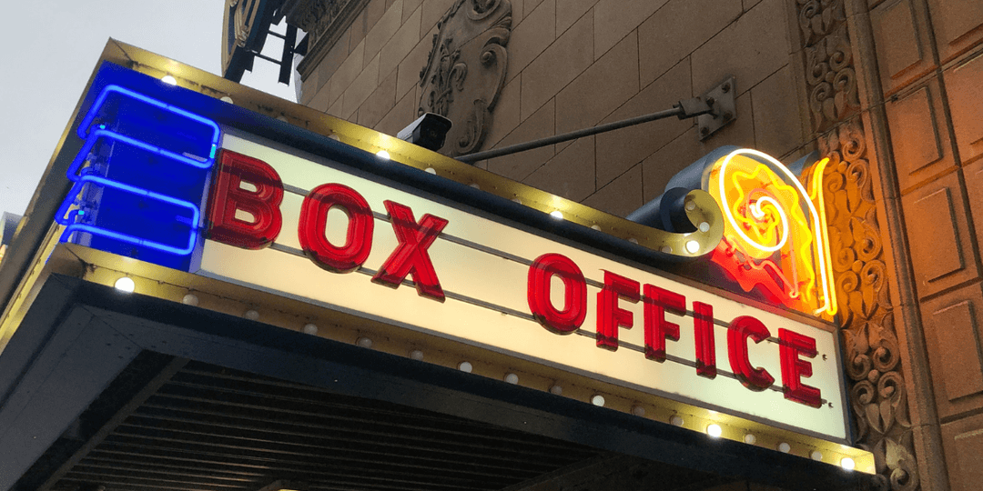 Neon box office sign illuminated in vibrant colors above a theater entrance