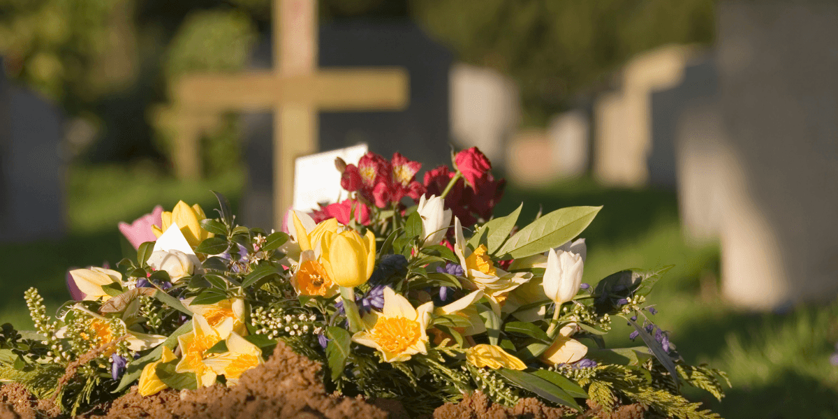 Vibrant flower arrangements on fresh earth at a cemetery with gravestones in the background