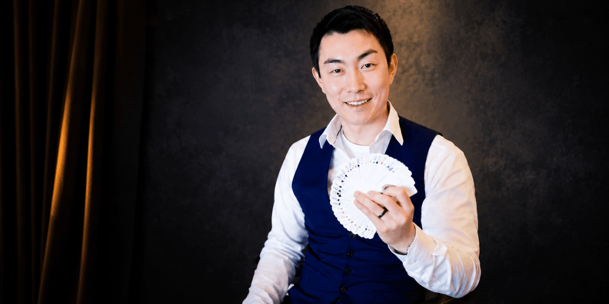 Man in a vest holds a fan of playing cards, smiling at the camera