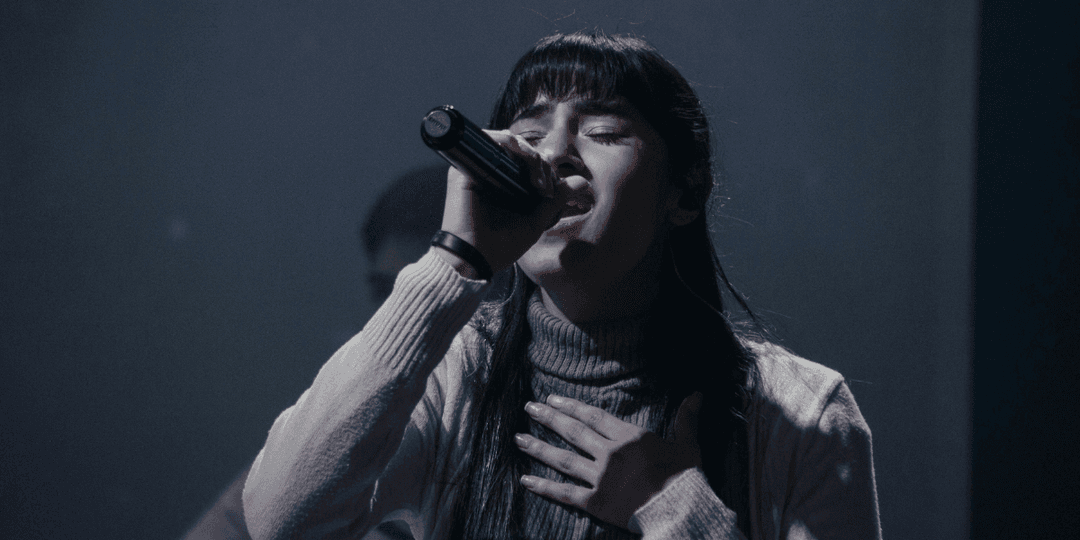 A singer passionately performs on stage, holding a microphone and expressing deep emotion