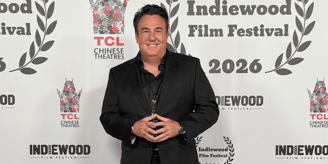 A man in a black suit poses at the Indiewood Film Festival backdrop