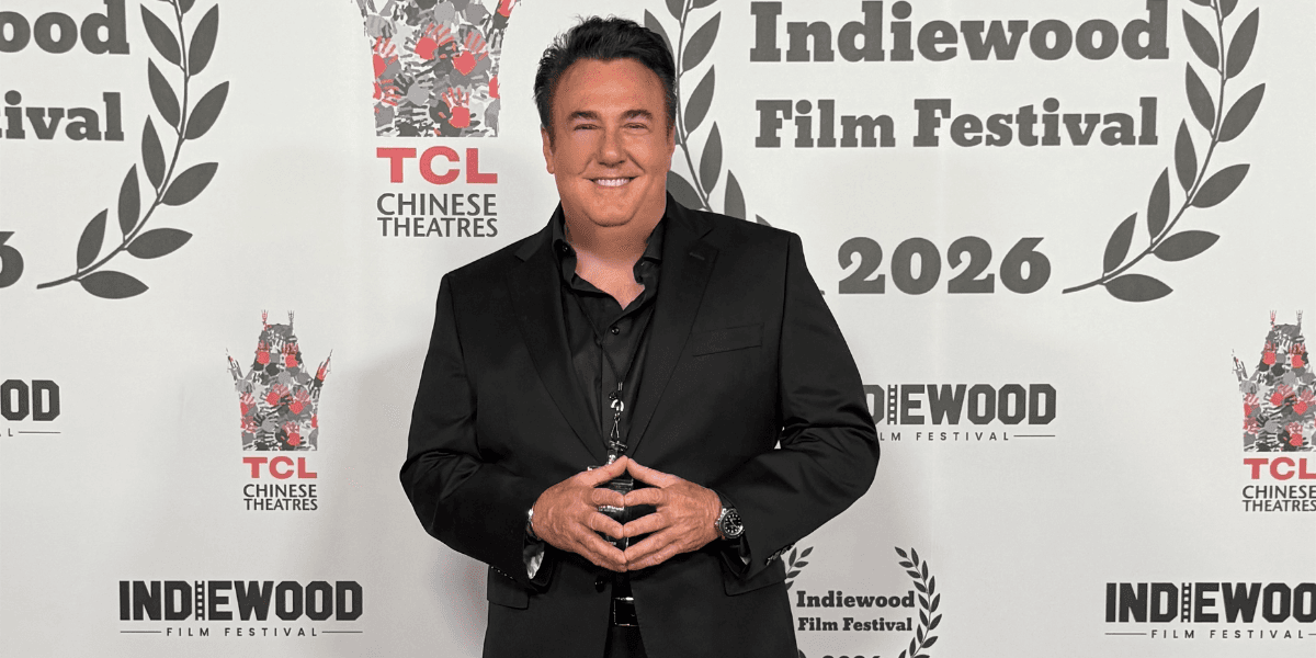 A man in a black suit poses at the Indiewood Film Festival backdrop