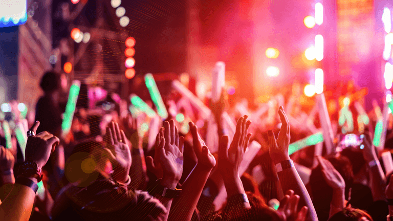 Crowd cheering with raised hands and glow sticks during a live outdoor music concert.