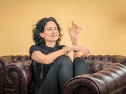 Elle Pirmoradi seated on a leather sofa holding a Bangelle gold bangle.