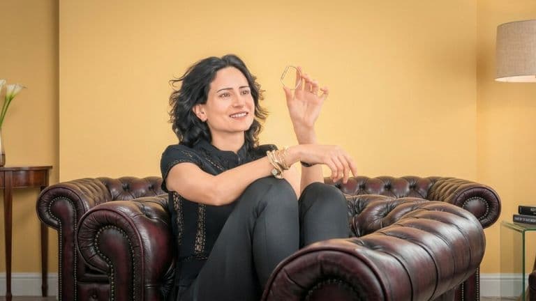 Elle Pirmoradi seated on a leather sofa holding a Bangelle gold bangle.