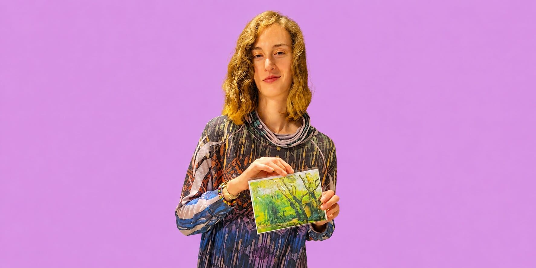 Tomiko Kausal-Hayes holding a colorful nature art print against a purple background.