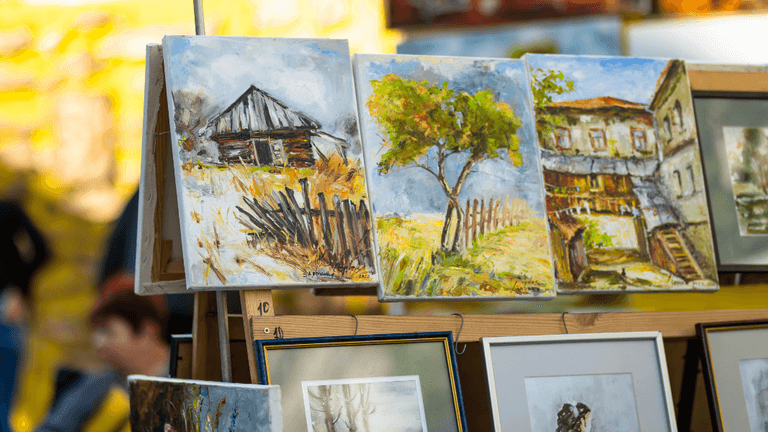 Landscape paintings displayed on outdoor easels at the Ann Arbor Art Fair.