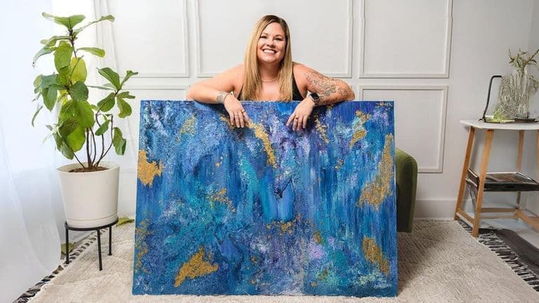 Traci Pearce smiles while holding a vibrant blue and gold abstract painting, showcasing her artistic journey and passion.