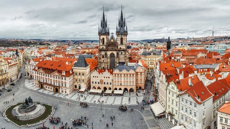 Panoramic view of Prague's Old Town Square with its distinctive red rooftops and the Gothic spires of Týn Church.