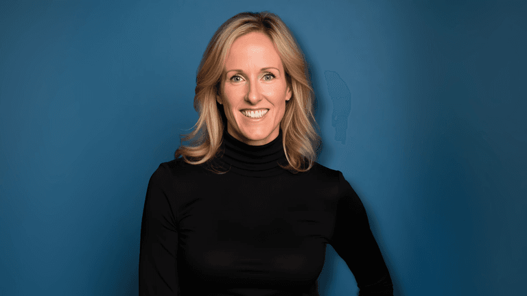 Erica Haupert smiling in a black turtleneck against a solid blue background.