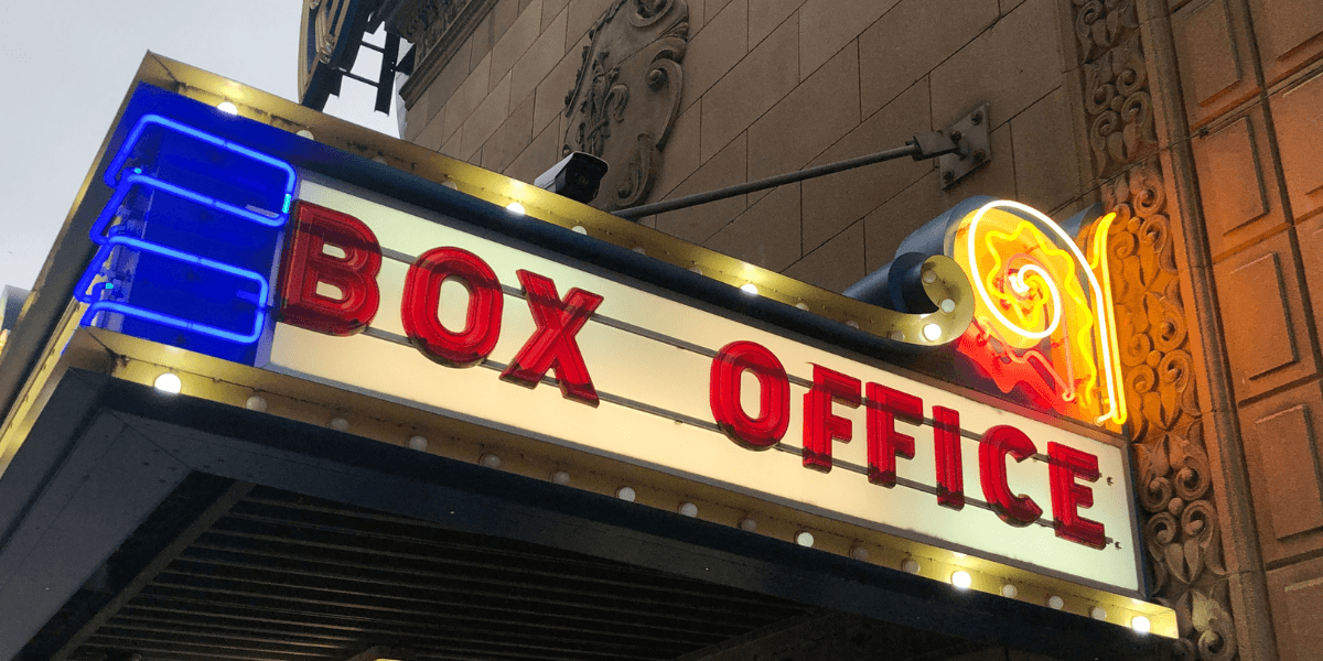 Neon box office sign illuminated in vibrant colors above a theater entrance