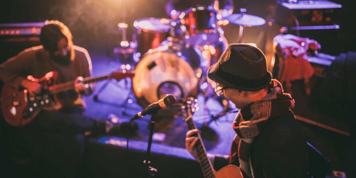 Two musicians performing on stage with instruments surrounded by colorful stage lighting