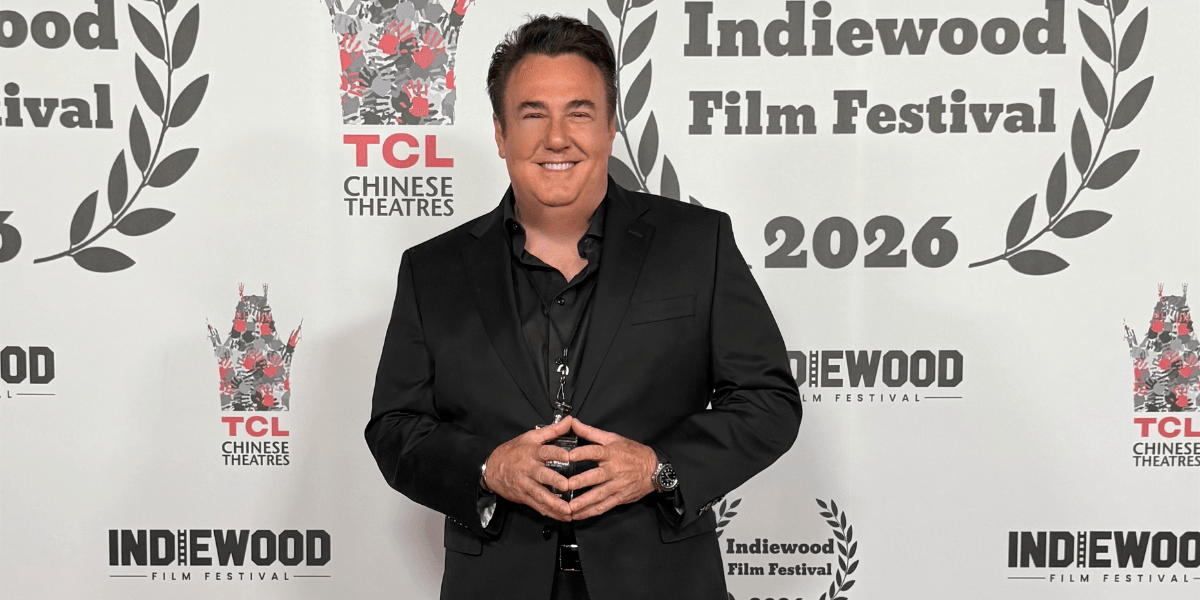 A man in a black suit poses at the Indiewood Film Festival backdrop