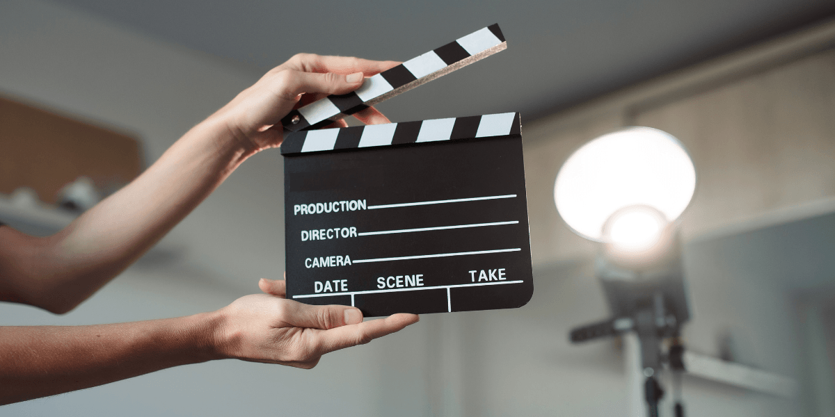 A person holding a movie clapboard with lighting equipment in the background