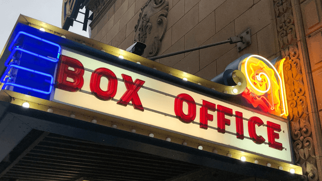 Neon box office sign illuminated in vibrant colors above a theater entrance