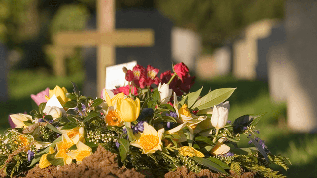 Vibrant flower arrangements on fresh earth at a cemetery with gravestones in the background