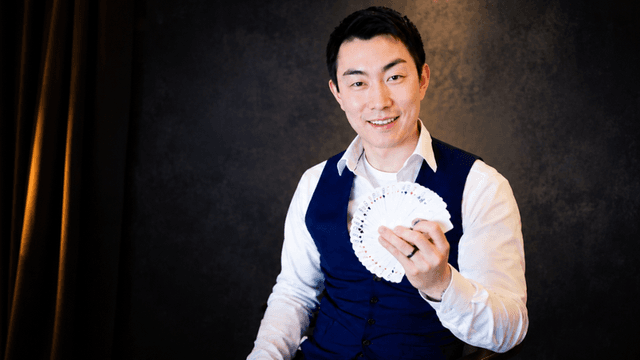 Man in a vest holds a fan of playing cards, smiling at the camera