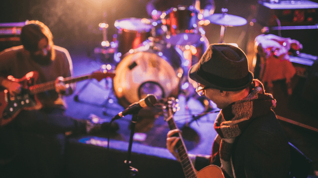 Two musicians performing on stage with instruments surrounded by colorful stage lighting