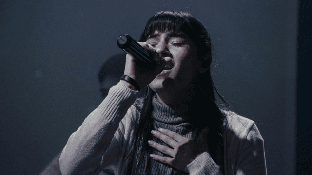 A singer passionately performs on stage, holding a microphone and expressing deep emotion