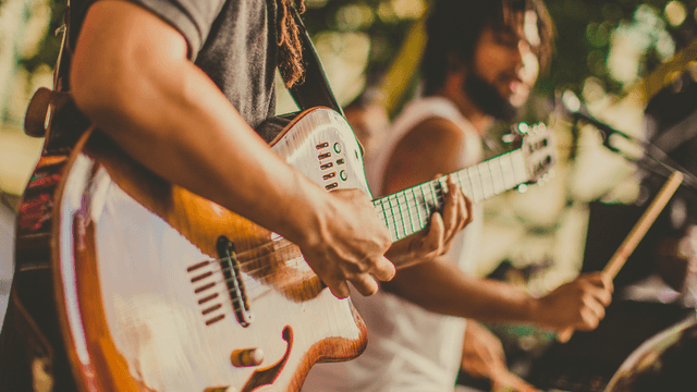 Musicians performing on stage, focusing on guitar and drums amidst a vibrant atmosphere