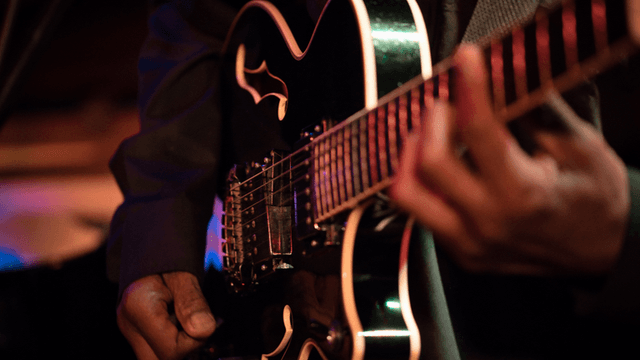 Close-up of a musician playing an electric guitar on stage with vibrant lighting