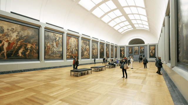 Interior of an art gallery with large paintings and visitors observing the art