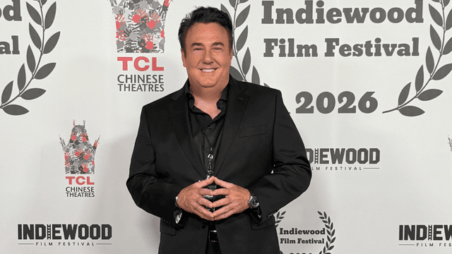 A man in a black suit poses at the Indiewood Film Festival backdrop