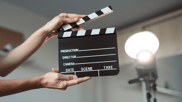 A person holding a movie clapboard with lighting equipment in the background