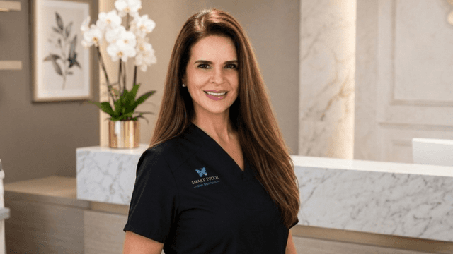 Smiling professional woman in a black uniform stands in a modern clinic reception area