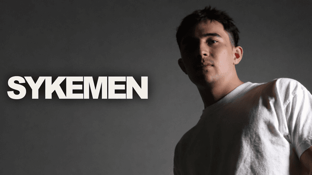 A young man in a white shirt poses against a dark background with stylized text.