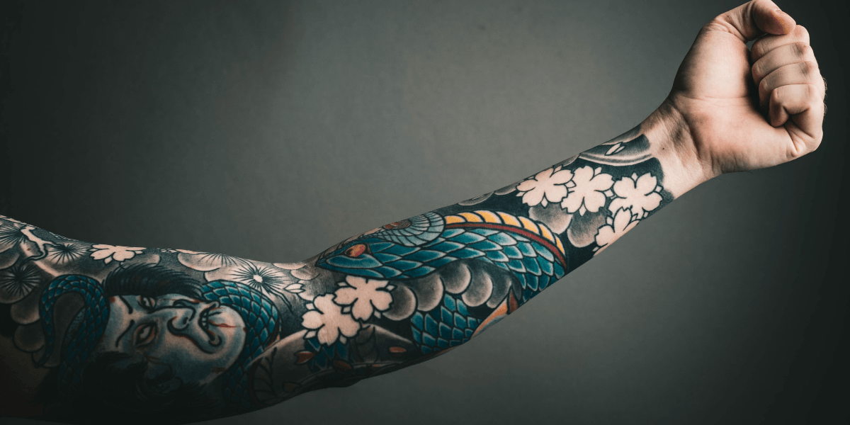Colorful Japanese-style tattoo sleeve featuring a serpent, flowers, and portrait on an outstretched arm.