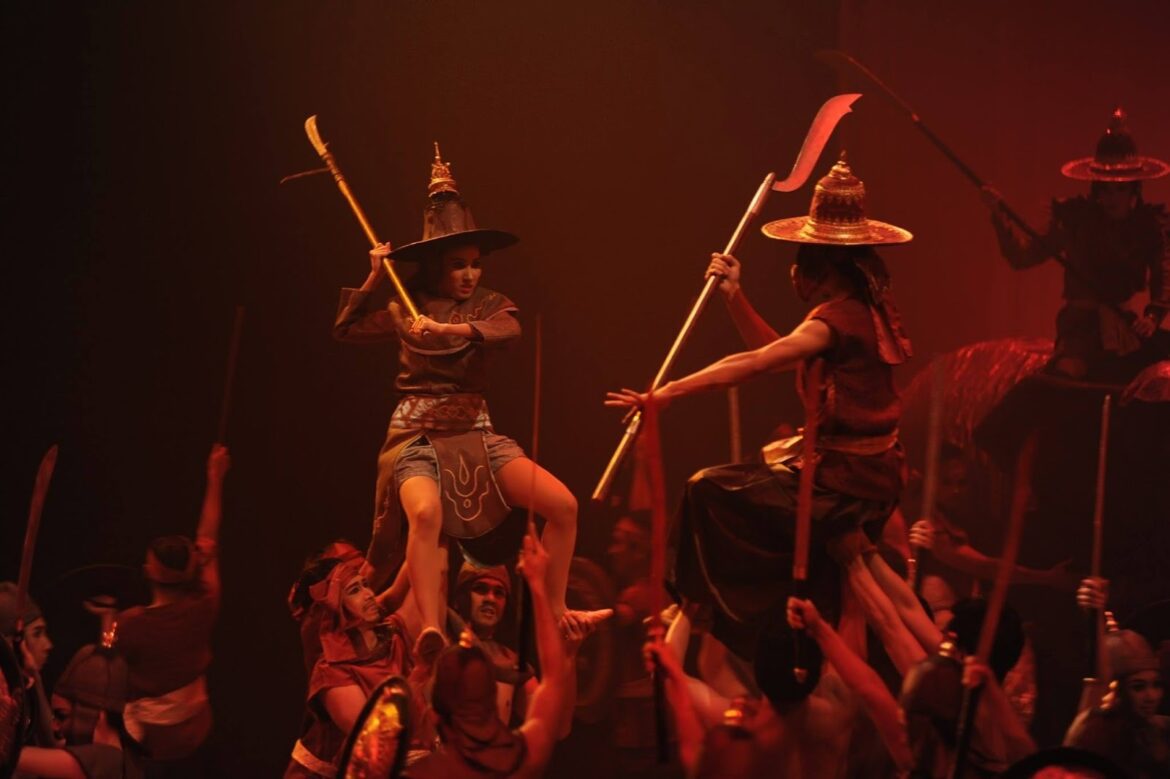 Scene from Somtow’s ballet Suriyothai, with dancers in dramatic battle poses honoring Thailand’s Queen Mother through performance.