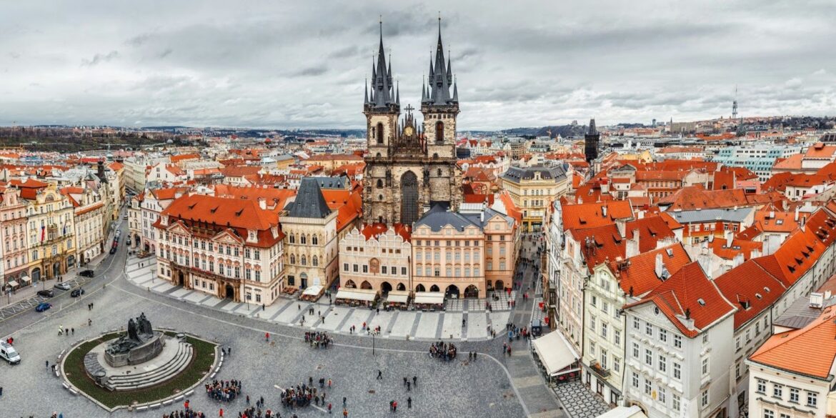 Panoramic view of Prague's Old Town Square with its distinctive red rooftops and the Gothic spires of Týn Church.