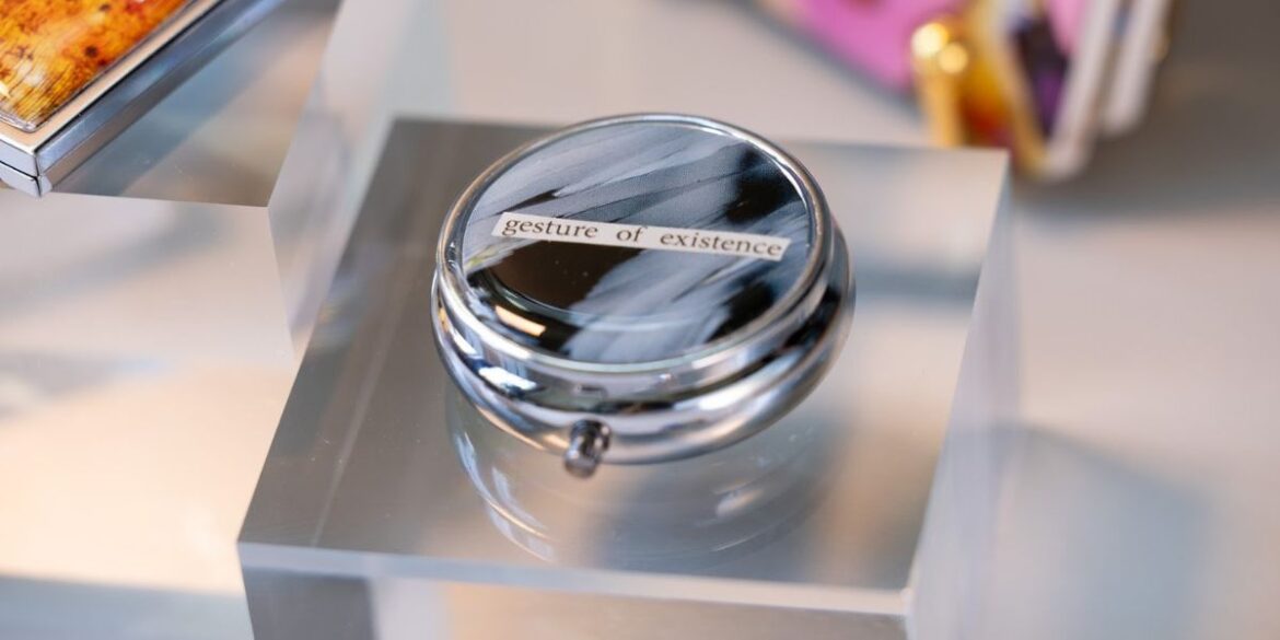 a pillbox with the phrase "gesture of existence," blending scientific imagery with artistic design.