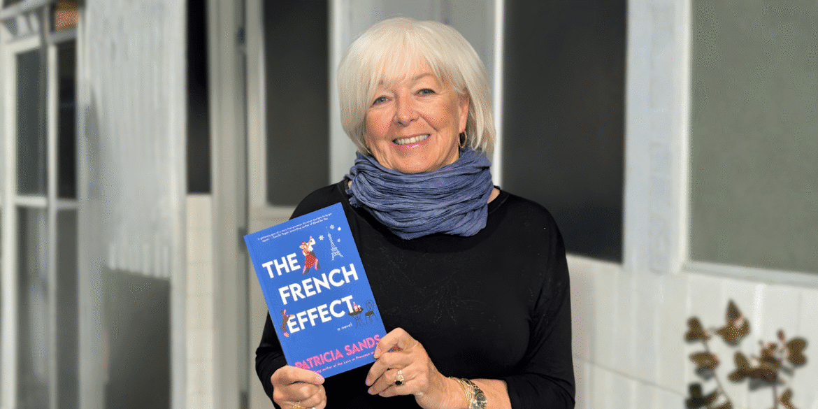 Patricia Sands holding her book *The French Effect*, smiling outdoors with a scarf and casual attire.