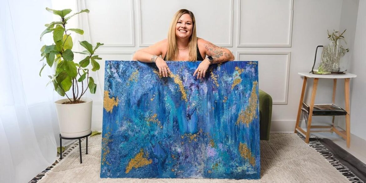 Traci Pearce smiles while holding a vibrant blue and gold abstract painting, showcasing her artistic journey and passion.