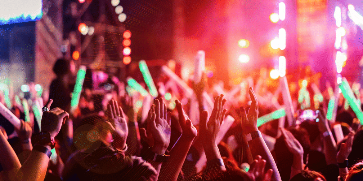 Crowd cheering with raised hands and glow sticks during a live outdoor music concert.