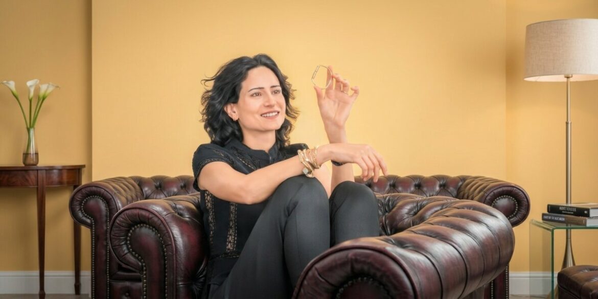 Elle Pirmoradi seated on a leather sofa holding a Bangelle gold bangle.